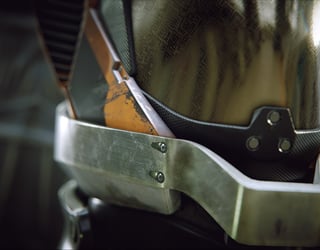 Armure métallique détaillée avec des marques d'usure, insérée dans un environnement flou et sombre.